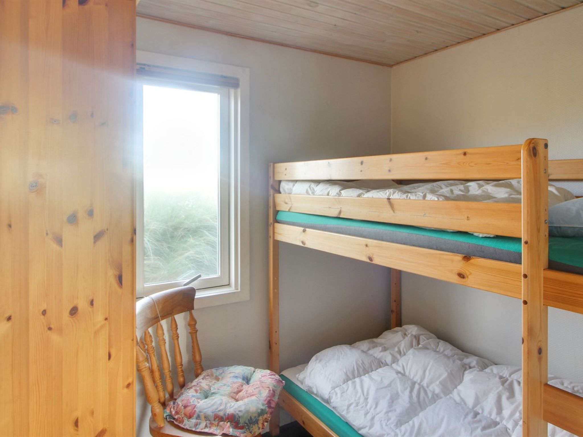 A bunk bed room with a window, a wooden chair, and a floral cushion.