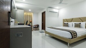 A hotel room with a bed, a desk, a chair, a television, and an air conditioning unit.