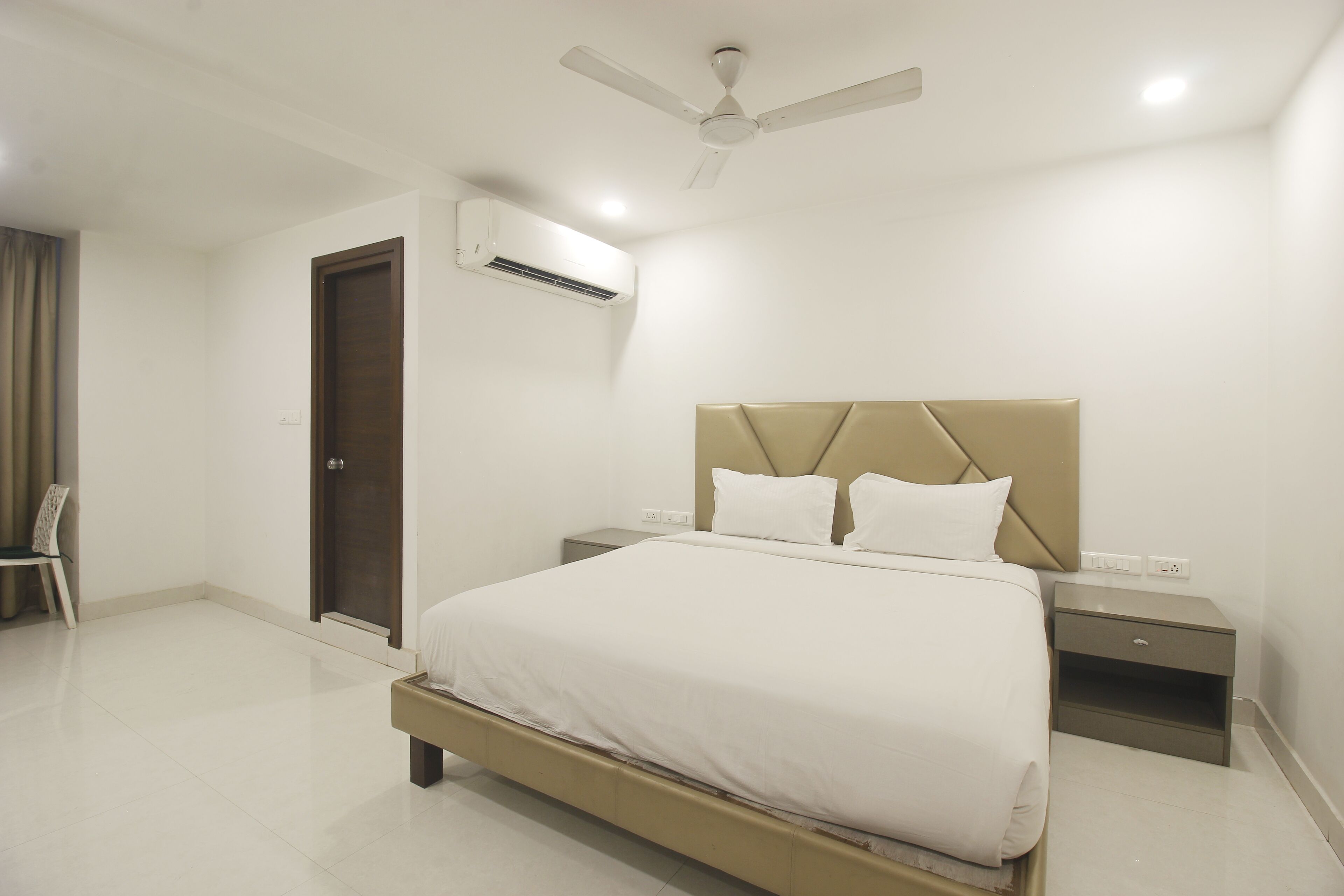A modern bedroom with a large bed, a bedside table, a nightstand, a ceiling fan, and an air conditioning unit.