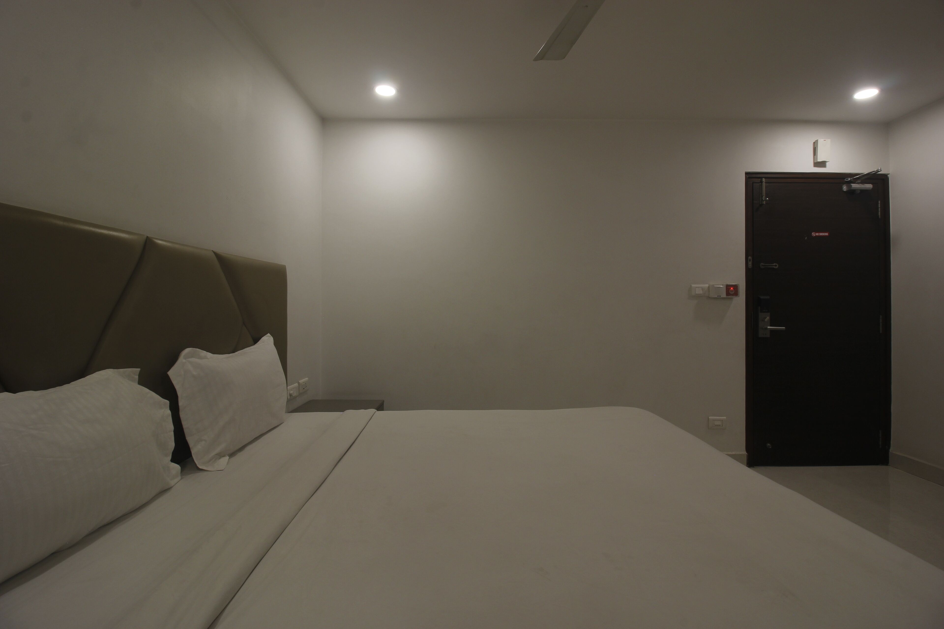 A hotel room with a large bed, a headboard, a door, and a light fixture on the ceiling.