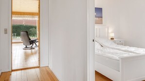 A modern bedroom with a wooden ceiling, a white bed, and a view of a balcony with a chair and a table. - "Rikhard" - 75m from the sea by Interhome (Dannemare)