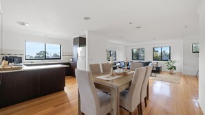 A modern kitchen with a central island, dining area with a wooden table and chairs, and a living room with a sofa and a coffee table. - The Island's Treasure (Cowes)