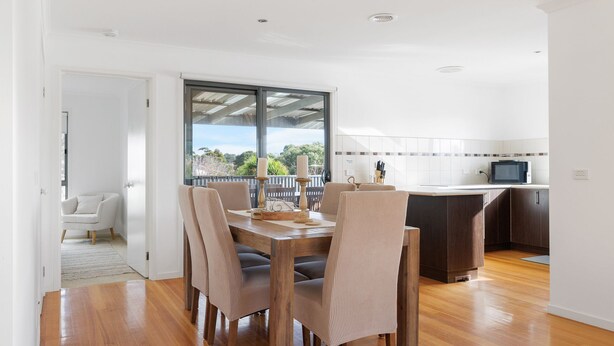 A modern kitchen with a microwave, a dining area with a wooden table and chairs, and a view of greenery outside. - The Island's Treasure (Cowes)