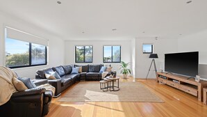 A modern living room with a sectional sofa, a flat-screen TV, and a large window offering a view of the outdoors. - The Island's Treasure (Cowes)