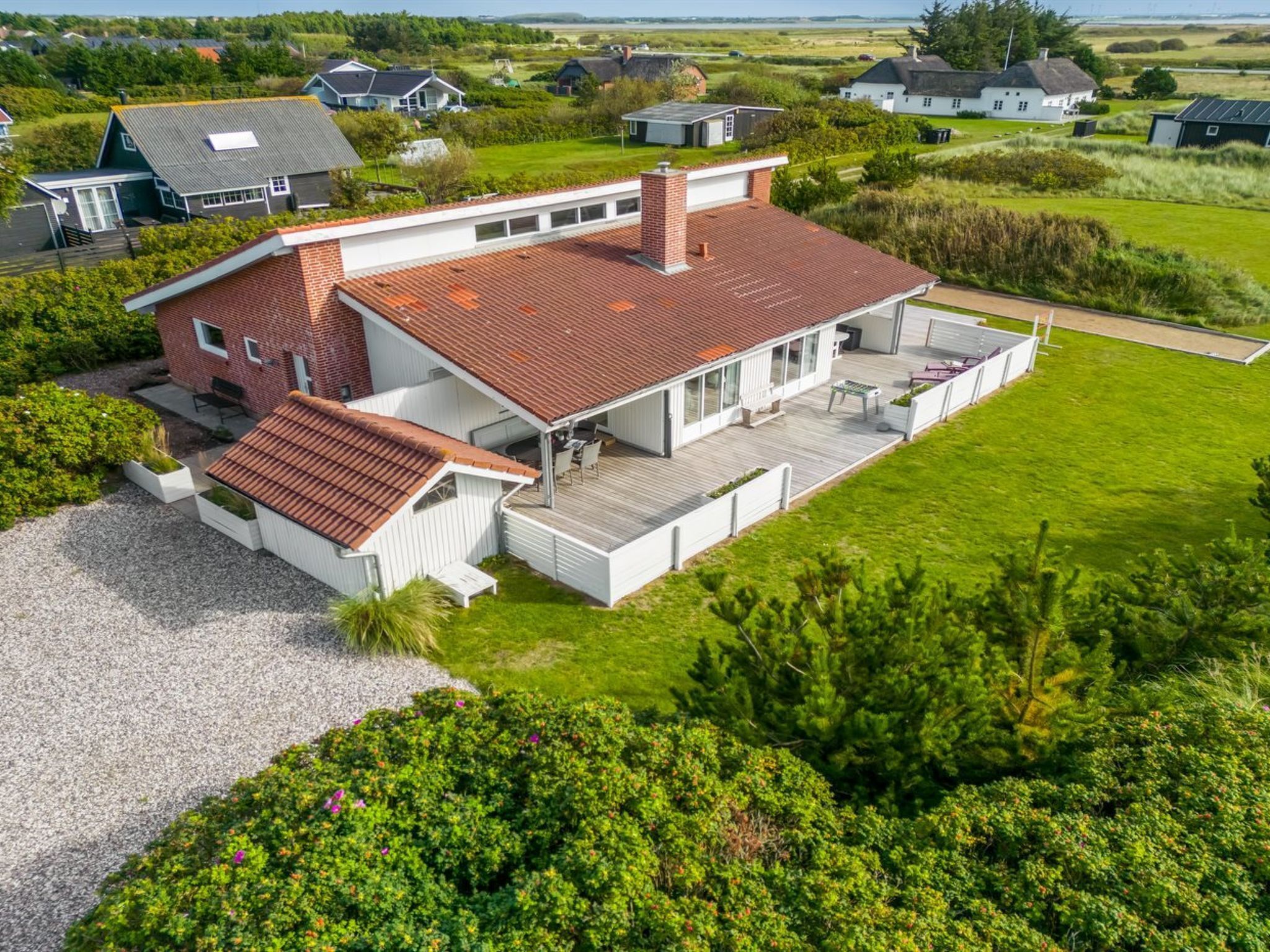 Een modern huis met een groot terras, omringd door weelderig groen en een verzorgd gazon.
