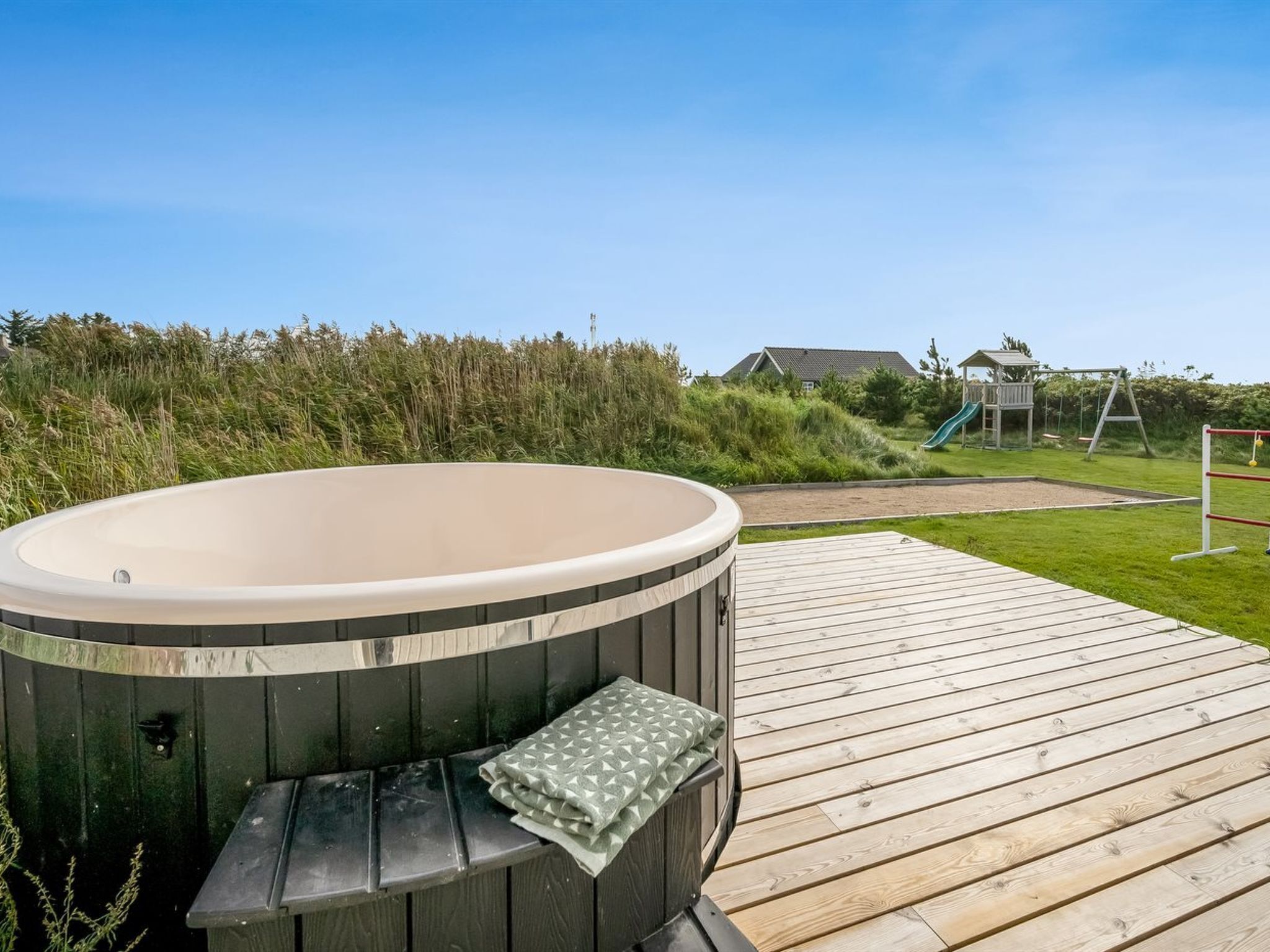 Un bain à remous sur une terrasse en bois, avec une pelouse et une aire de jeux en arrière-plan.