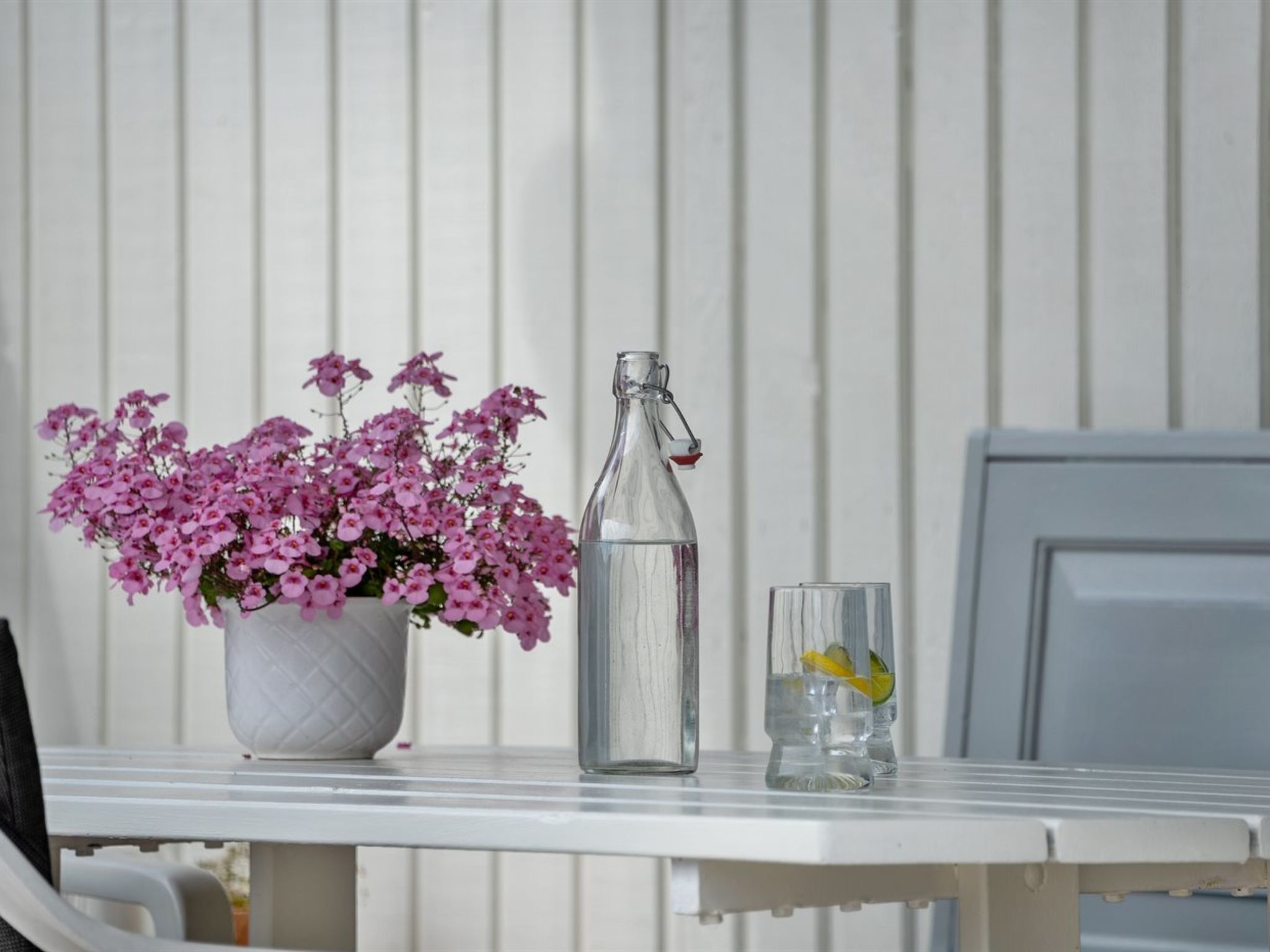 A white table with a clear glass bottle and a glass containing a slice of lemon.