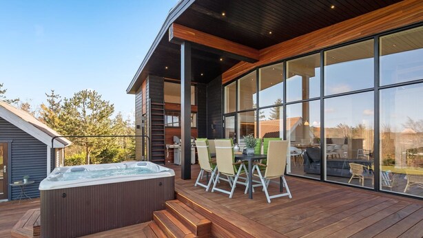 A modern outdoor deck with a hot tub, seating area, and large windows.