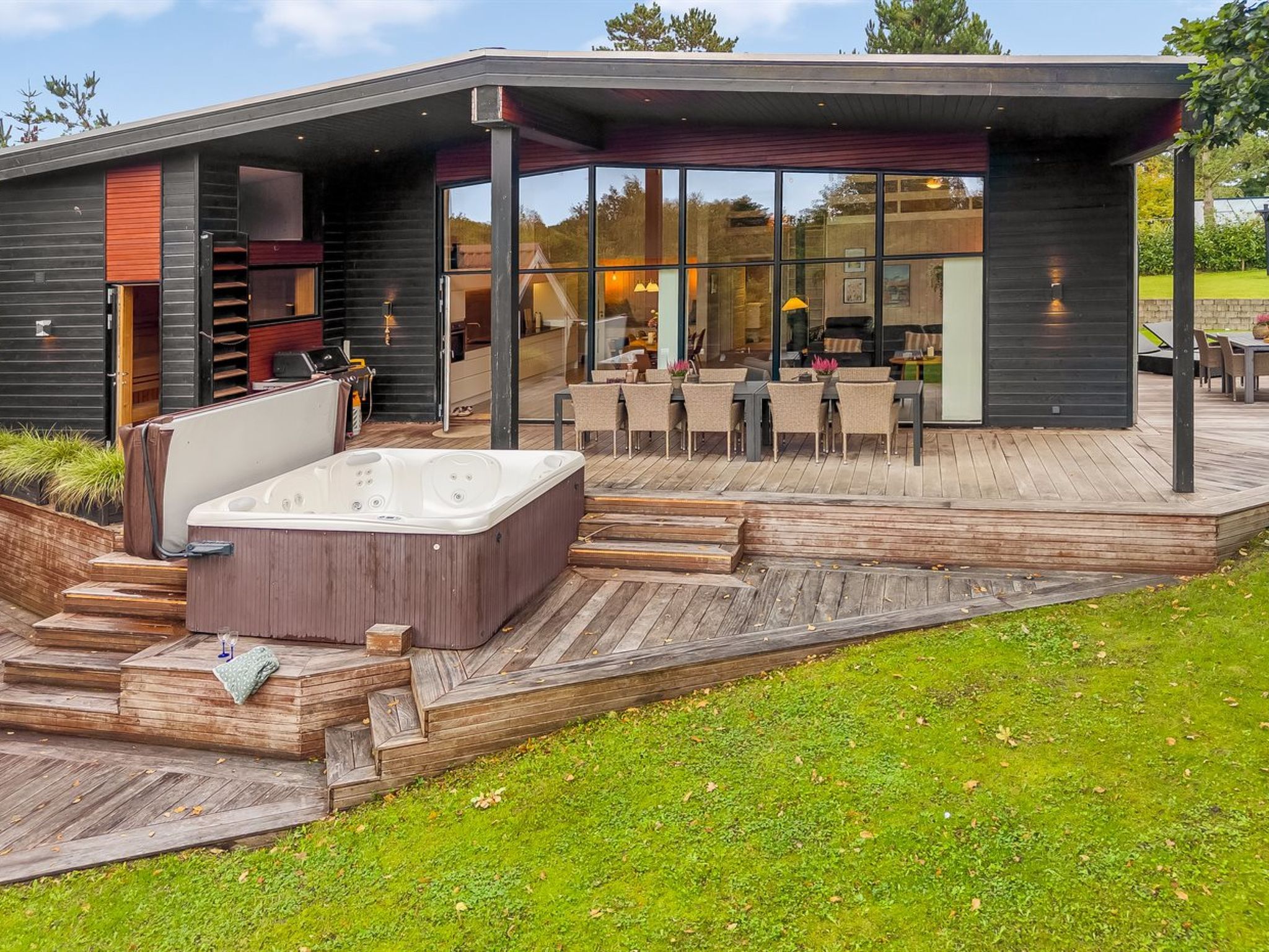 Un patio extérieur moderne doté d’un jacuzzi, d’une terrasse en bois et d’un espace salon couvert.