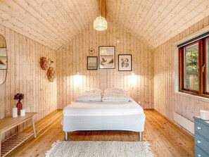 A wooden cabin bedroom with a bed, wall-mounted lights, and framed pictures.
