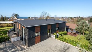 A modern two-story house with a dark exterior, a visible deck, and a clear view of the surrounding landscape.