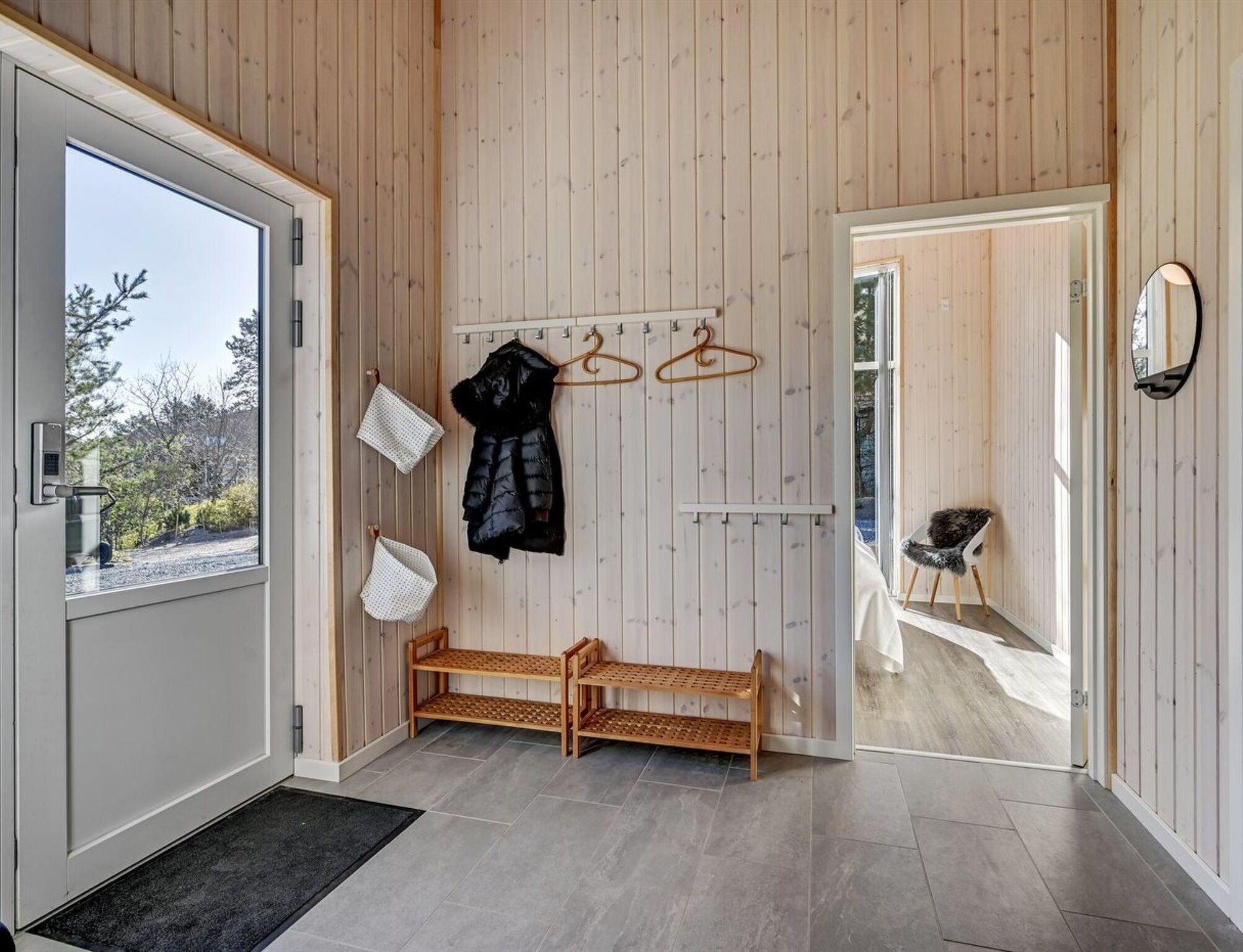 A modern interior with a wooden wall, a bench, a coat rack, and a mirror.