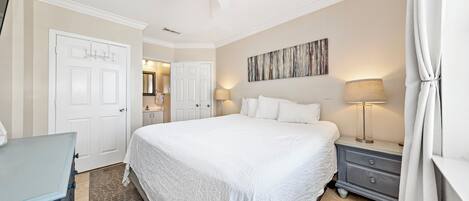 A bedroom with a large bed, a nightstand, a dresser, a ceiling fan, and a door.
