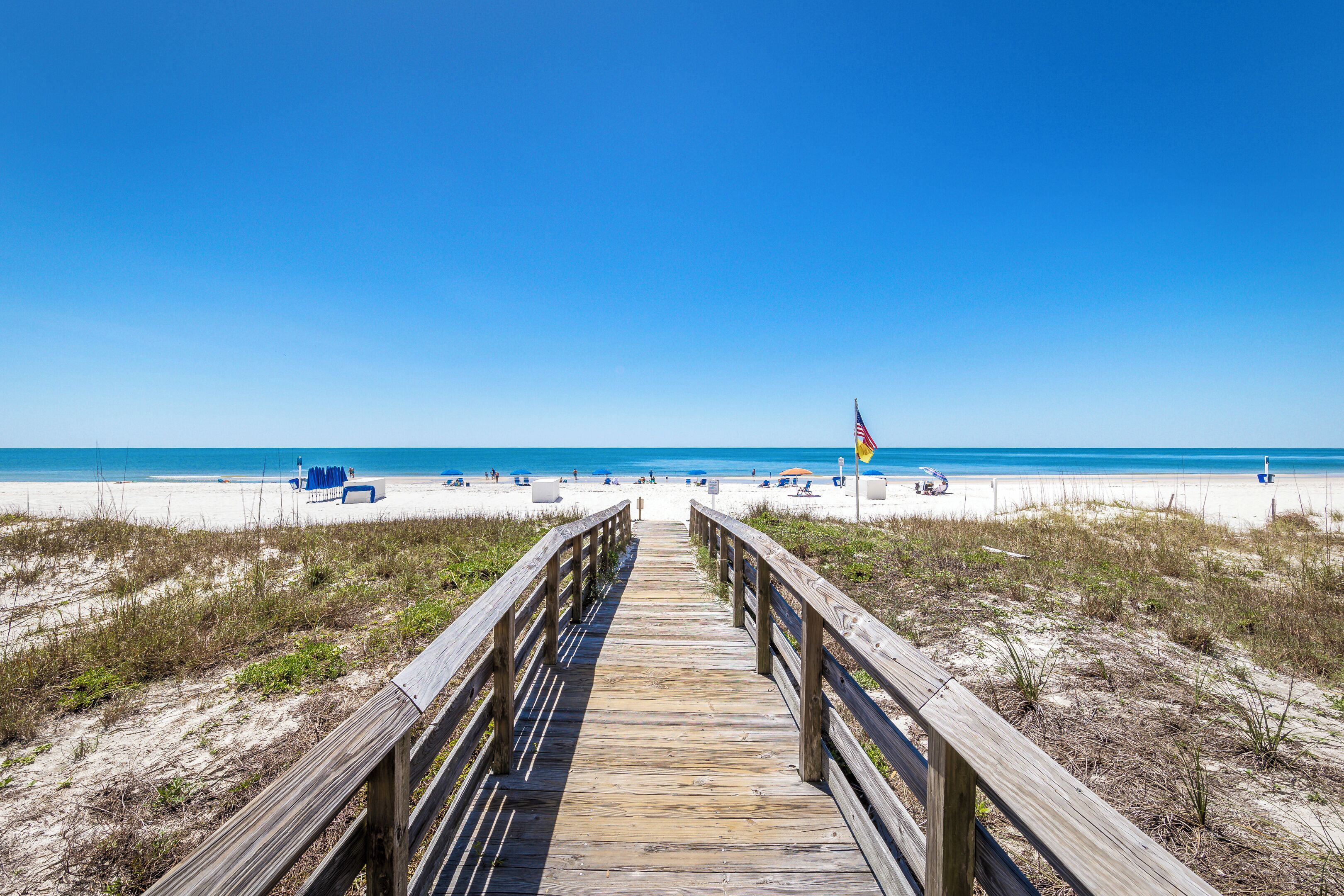 A wooden boardwalk leading to a beach with clear skies.