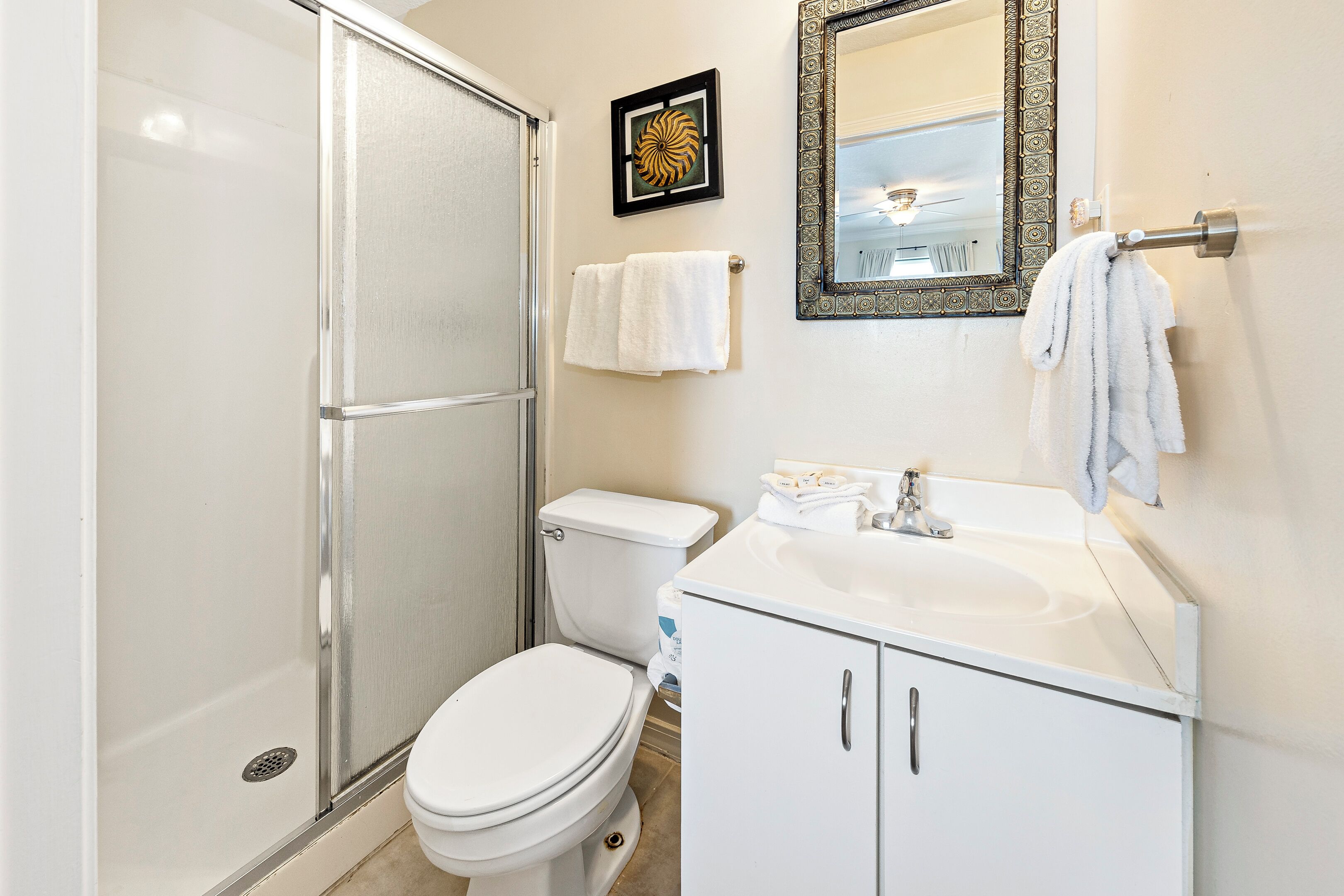 A bathroom with a shower, toilet, sink, and a mirror with a decorative frame.
