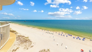 En strand med klart, blåt vand, en bro i det fjerne og strandparasoller.