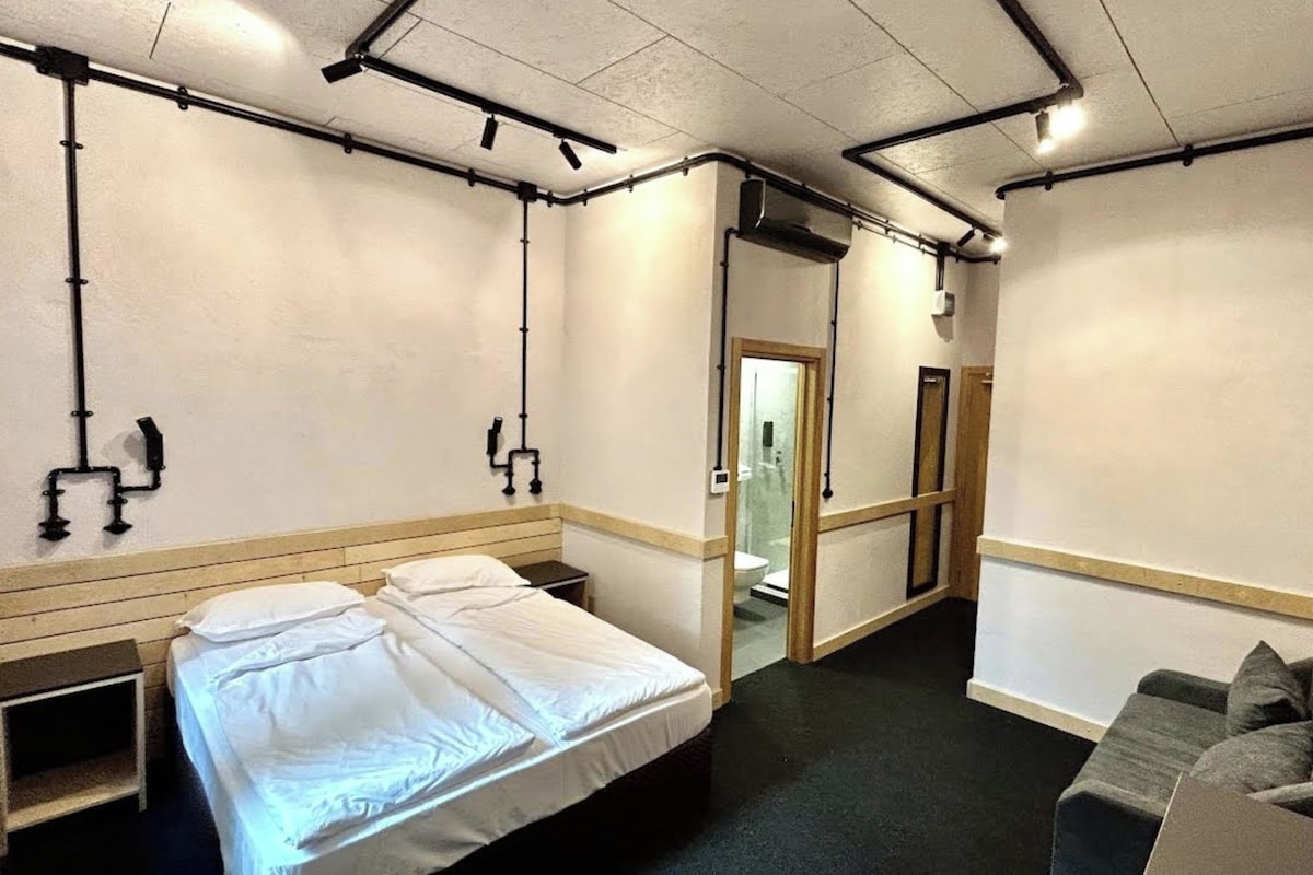 A hotel room with a bed, a sofa, and a bathroom visible through a doorway.