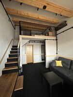 A loft-style apartment with a staircase leading to a mezzanine, a sofa, and a small table.