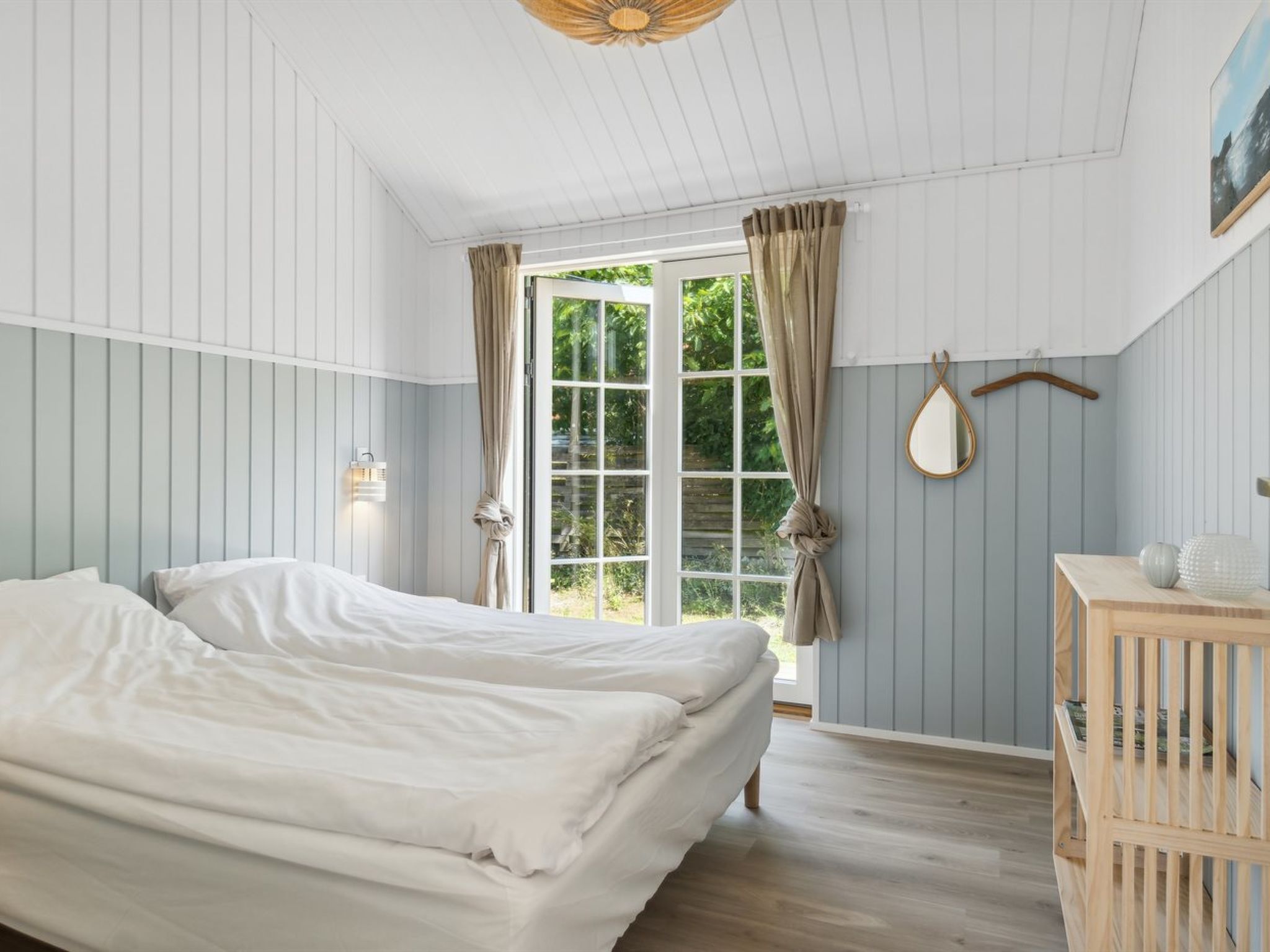 Un dormitorio con una cama, un aparador de madera, un espejo y una ventana con cortinas.