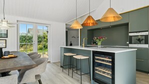 Une cuisine moderne dotée d’un îlot central, de luminaires suspendus et offrant une vue sur l’extérieur.