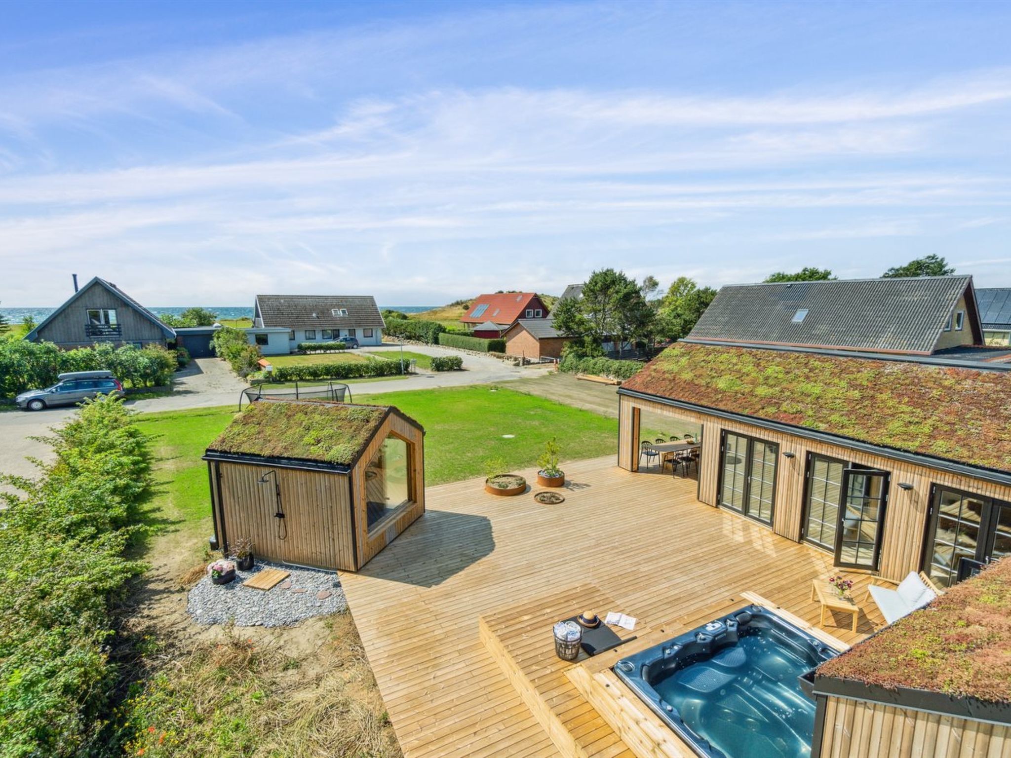 A modern house with a wooden deck, a hot tub, and a view of the sea.