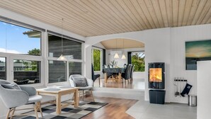 Ein modernes Wohnzimmer mit Holzboden, großen Fenstern, einem Essbereich und einem Kamin.