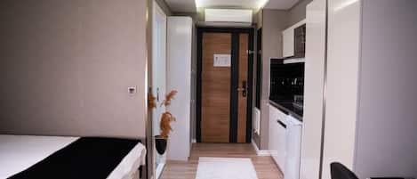 A narrow hallway with a bed on the left, a kitchenette on the right, and a door at the end.