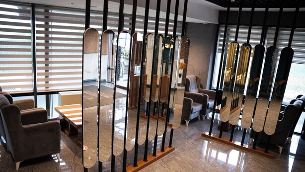 A modern interior with a reception desk, seating area, and a decorative partition with mirrors. - MG Hill Hotel (Malatya)