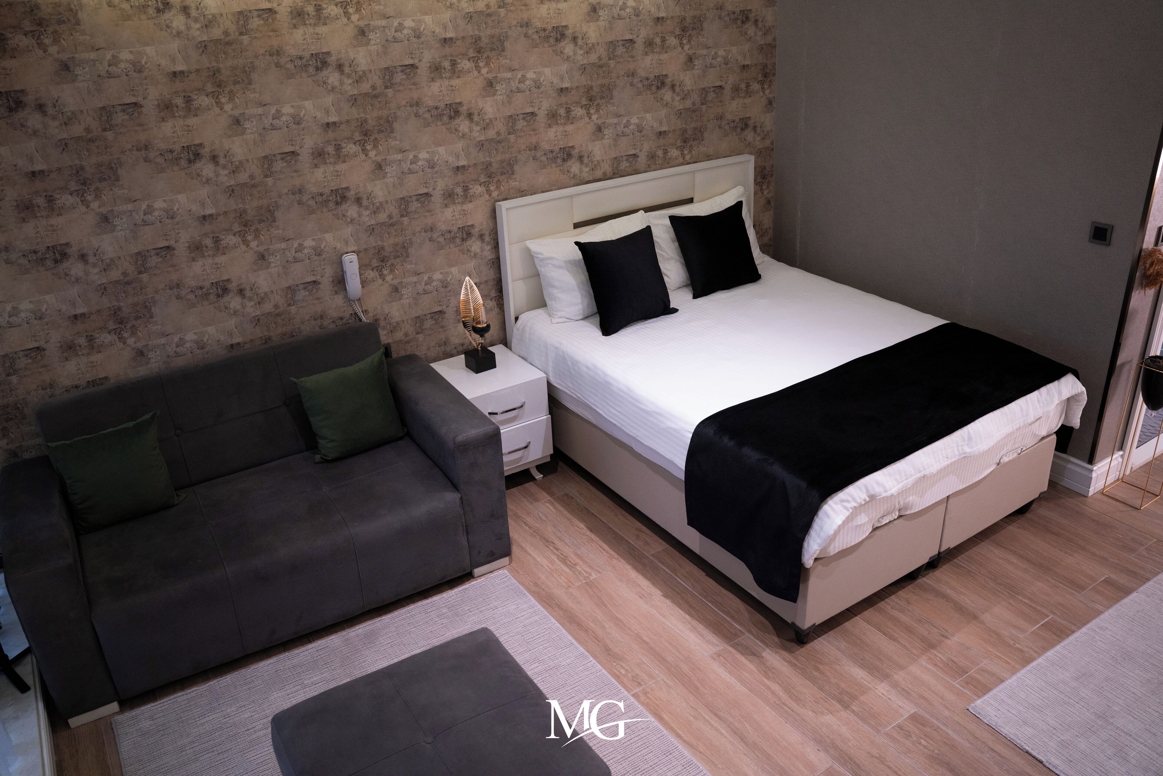 Un dormitorio con cama, mesita de noche, sofá y pared con diseño de ladrillo.
