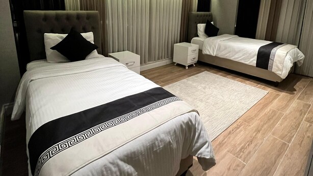 A modern bedroom with a large bed, a smaller bed, a nightstand, and a bedside table. - MG Hill Hotel (Malatya)