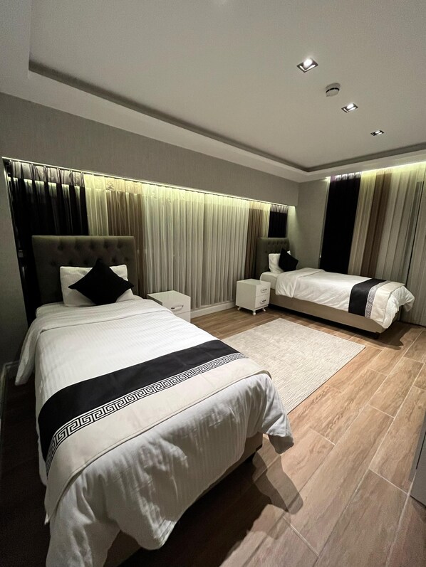 A modern bedroom with a large bed, a smaller bed, a nightstand, and a bedside table.