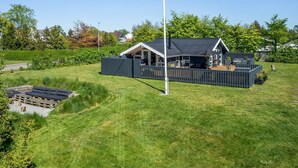 Een modern huis met een ruim terras, een vlaggenmast en een verzorgd gazon.