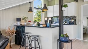 Een moderne keuken met een centraal eiland, krukken, hanglampen en uitzicht op de natuur.