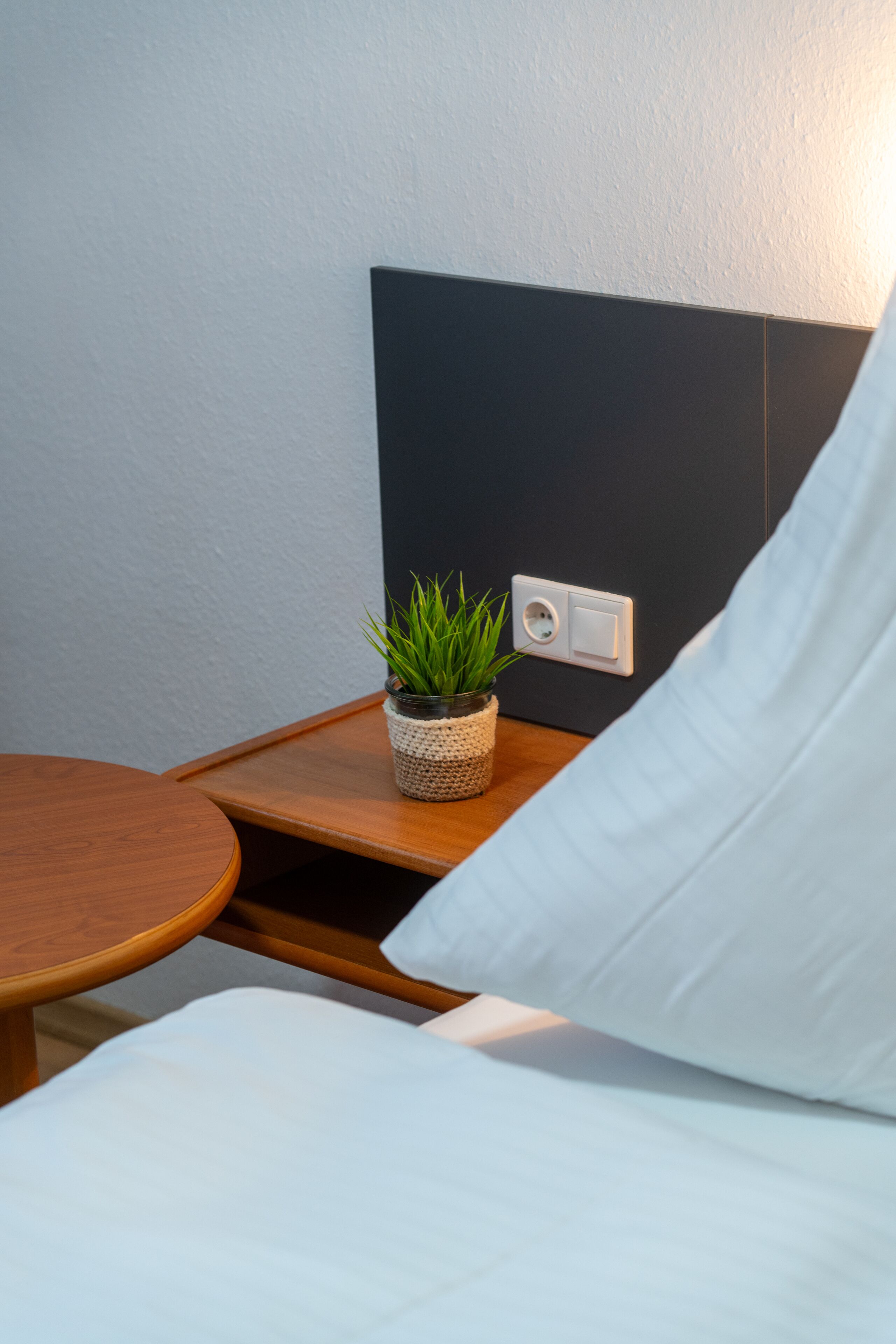 A neatly arranged bedroom with a bed, a bedside table with a potted plant, and a wall socket.