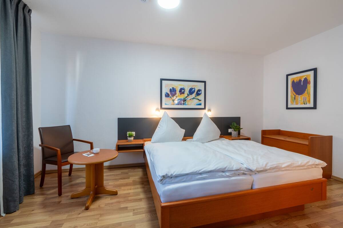 A hotel room with a wooden bed, a round table, a chair, and two wall-mounted lamps.