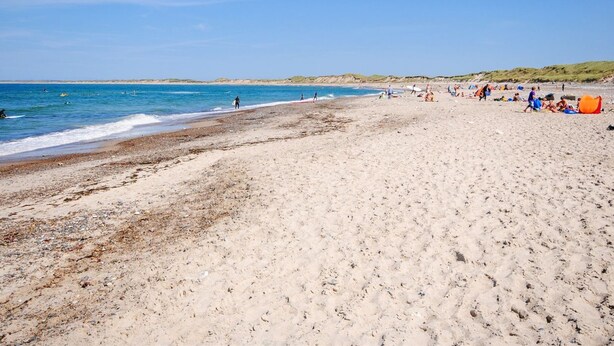 Ein weiter Sandstrand mit klarem, blauem Wasser, Menschen, die spazieren gehen, und ein paar aufgestellte Zelte.