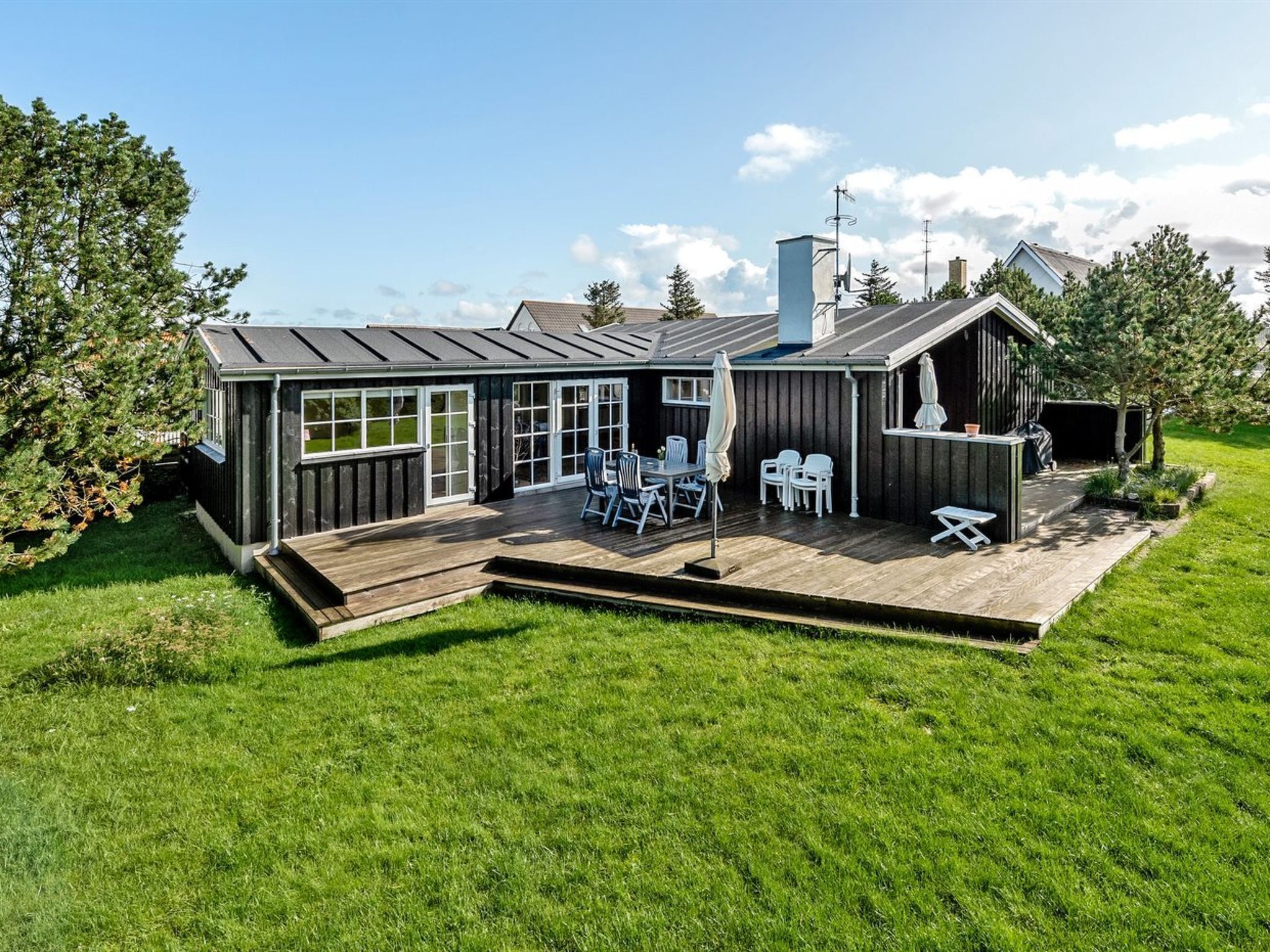 A modern house with a wooden deck, large windows, and outdoor seating.