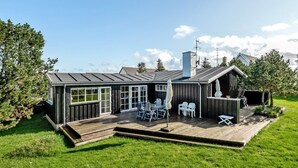 Ein modernes Haus mit einer Holzterrasse, großen Fenstern und Sitzgelegenheiten im Freien.