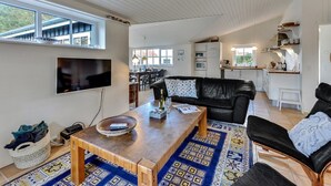 Ein großzügiger Wohnbereich mit einem Holztisch, einer schwarzen Ledersofa und einem gemusterten Teppich.