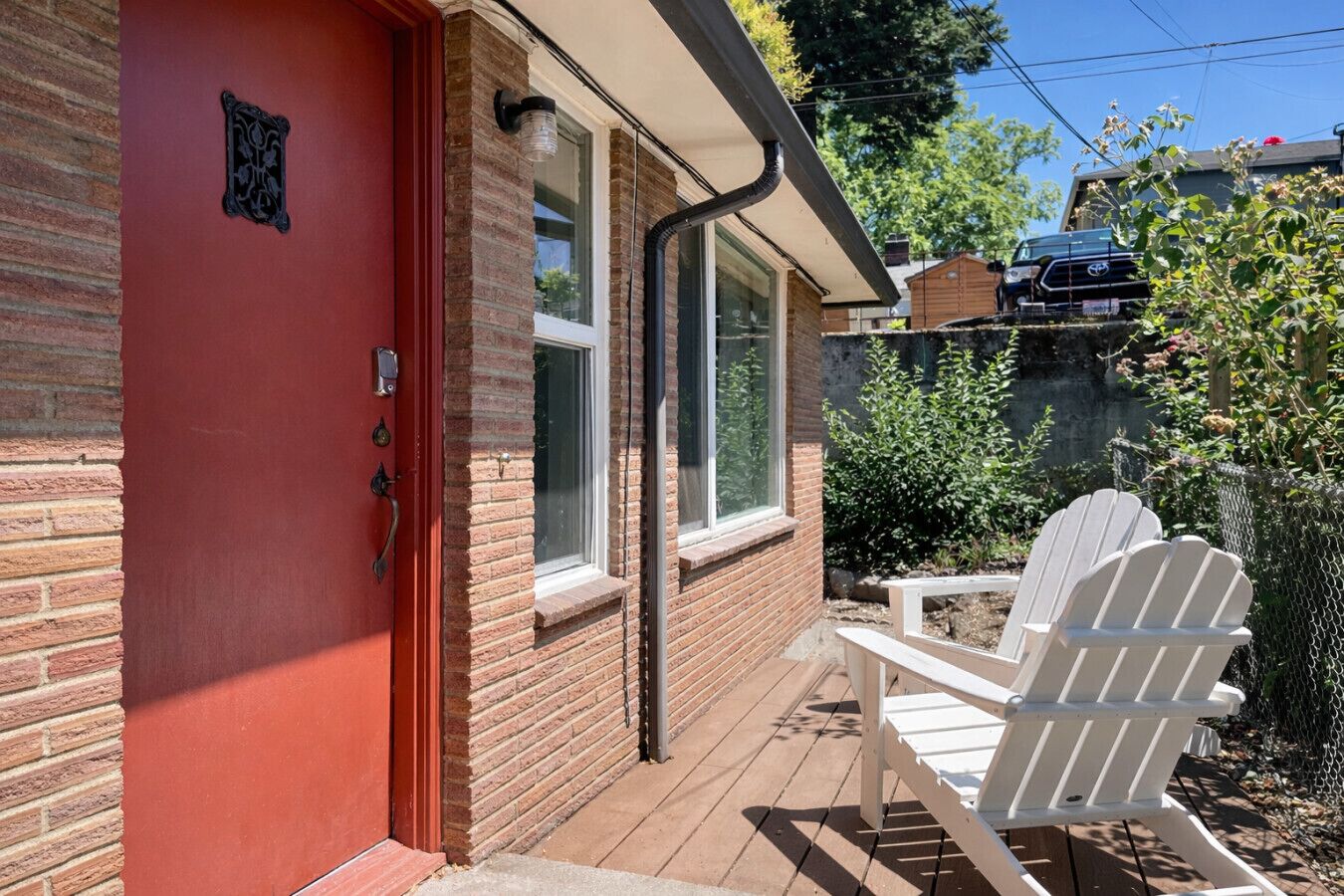 A red door with a small window, a white chair outside, and a brick wall.
