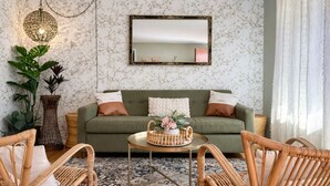 Una sala de estar acogedora con un sofá verde, sillas de mimbre, una mesa redonda y una lámpara colgante.