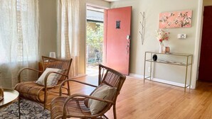 A room with two wicker chairs, a small table, a console table with decorative items, and a door leading outside. - Fremont Nirvana | Chic Townhome Near Bars & Eats (Seattle)