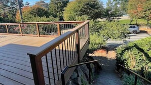 A wooden deck with a metal railing, a stone pathway, and a car parked in the background. - Fremont Nirvana | Chic Townhome Near Bars & Eats (Seattle)