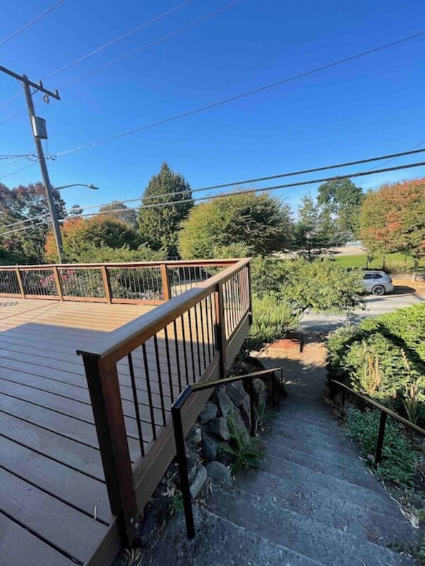 A wooden deck with a metal railing, a stone pathway, and a car parked in the background.