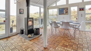 Un intérieur moderne avec un poêle à bois, des murs blancs et un coin repas comprenant des chaises et une table.