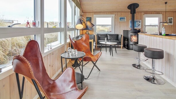 Une pièce spacieuse dotée de grandes fenêtres, d’un plafond en bois, d’une cheminée et d’un coin bar.