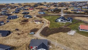 Une vue aérienne d’un village côtier, avec des maisons, une route et une plage en arrière-plan.