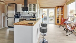 Une cuisine moderne avec des meubles en bois, un réfrigérateur en acier inoxydable et une machine à café. Une grande fenêtre offre une vue sur l’extérieur.