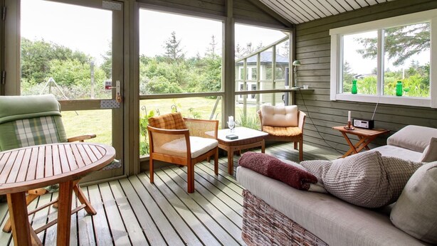 A covered outdoor seating area with wooden furniture, a table, and a sofa.