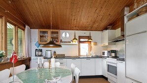 A modern kitchen with wooden ceiling, white cabinets, stainless steel appliances, and a dining area with a table and chairs.